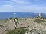 Senderista camina hacia el **puerto de Navafría**, con un mojón y montañas nevadas al fondo.