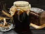 Słoik z ciemnym płynem, chleb żytni i kłosy zboża. Idealne składniki do domowego kwas chlebowy przepis.