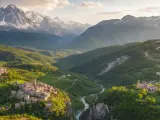 Borghi antichi aggrappati a colline verdi, un fiume azzurro scorre tra valli profonde, con il maestoso monte in Abruzzo che domina l'orizzonte innevato.