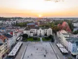 Zachód słońca nad rynkiem, gdzie widać piękną pierzeję kamienic i ratusz. Ludzie spacerują po placu, ciesząc się ciepłym wieczorem.