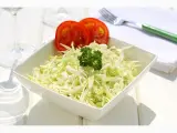 Frischer, selbstgemachter Krautsalat in einer weißen Schüssel, garniert mit Petersilie und Tomatenscheiben. Daneben liegen ein grüner Löffel und eine Serviette.