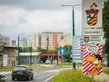Znak drogowy "Sosnowiec" i humorystyczny napis "Paszport masz?!" przy wjeździe do miasta. W tle bloki mieszkalne.