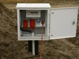 Skrzynka elektryczna na działce bez domu, gotowa do podłączenia prądu. Widoczne gniazda i zabezpieczenia.