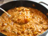 Cuchara llena de cremoso arroz con pollo de la abuela, humeante y con trozos de pollo y champiñones.