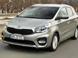 Srebrny Kia Carens, typowy MPV, jedzie po drodze. To auto rodzinne, idealne na wycieczki.
