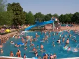 Ein belebtes Freibad in Goslar mit vielen Menschen, die im Wasser planschen und die blaue Wasserrutsche genießen.