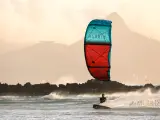 Kitesurfer na desce w akcji, z kolorowym latawcem na tle gór i morza.