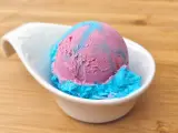 Ein Löffel eis mit kaugummi Geschmack, in rosa und blau, serviert in einer weißen Schale auf Holzuntergrund.