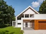 Nowoczesny dom z drewnianą bramą garażową i dużymi oknami, otoczony zielenią. Ta kategoria obiektu budowlanego zachwyca.
