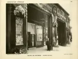 Façade de galerie de boutiques, style art déco, avec ornements floraux et motifs circulaires. Un homme en costume se tient sur le trottoir.