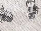 Tre solstolar i trä står på en sliten altan. Solen kastar långa skuggor över siox trall.