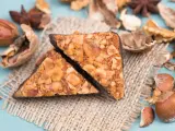 Zwei vegane Nussecken mit Schokoladenrand, bedeckt mit gehackten Nüssen, liegen auf einem Jutesack, umgeben von verschiedenen Nüssen und Sternanis.