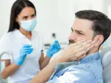 Mężczyzna z bólem policzka u dentysty, który bada jego dziąsła. Może to być objaw problemów z kieszonkami dziąsłowymi.