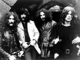 Członkowie zespołu Black Sabbath pozują do zdjęcia w mrocznym otoczeniu.