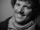 Uśmiechnięty Filip Ćwik w szarym szaliku, z kręconymi włosami i zarostem.