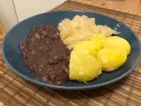 Ein Teller mit deftigem Essen: dunkle Soße, Sauerkraut und Salzkartoffeln. Erinnert an die gute, alte tote Oma.