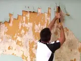 Man scraping old wallpaper off a wall.