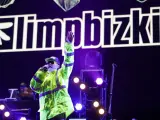 Fred Durst z Limp Bizkit na koncercie, w neonowej kurtce, z ręką w górze. Tło to logo zespołu.