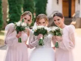 Trzy uśmiechnięte kobiety z bukietami kwiatów. Panna młoda w białej sukni i dwie druchny w różowych sukienkach.