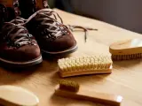 Brązowe zamszowe buty i kilka szczotek na drewnianym stole. Idealne akcesoria, by dowiedzieć się, jak wyczyścić zamszowe buty.