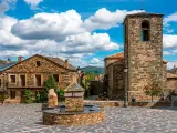 Plaza con fuente de piedra y campanario en un pueblo de la ruta negra Guadalajara. Casas de piedra y cielo azul con nubes.
