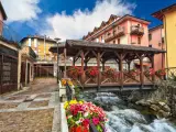 Un pittoresco ponte di legno coperto, adornato di fiori, attraversa un torrente impetuoso. Un incantevole scorcio di cosa vedere in un borgo alpino.