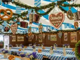 Wnętrze namiotu na Oktoberfest w Monachium. Wiszące precle, serca z piernika i akordeony. Stoły przykryte niebiesko-białymi obrusami, ozdobione kwiatami i kolejnymi preclami.