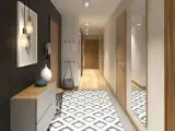 Un corridoio stretto con un tappeto geometrico, mobili moderni e un quadro astratto. Idee per un corridoio che unisce funzionalità ed estetica.