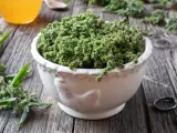 Schale mit Brennesselsamen, die ihre positive brennesselsamen wirkung für die Gesundheit andeuten. Daneben ein Glas mit gelber Flüssigkeit.