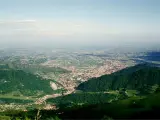 Vista panoramica dalla sella di Fadalto su una vasta pianura punteggiata di case e campi, con colline verdi in primo piano.