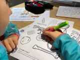 Dziecko koloruje edukacyjne karty pracy z dinozaurem i artefaktami.