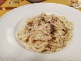 Pici cacio e pepe, un classico piatto romano, servito in un piatto bianco, con abbondante pepe nero macinato.
