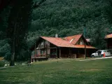 Drewniany domek w górach, idealne miejsce na letni weekend. Dwa samochody zaparkowane przed domem, otoczonym zielenią i lasem.