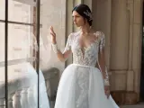 Panna młoda w sukni ślubnej z koronką i trenem, z ozdobną fryzurą w stylu bollywood, patrzy przez okno.