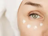 Augenpartie mit feinen Linien, die auf erste Falten unter den Augen mit 20 hindeuten. Cremepunkte unter dem Auge für Pflege.