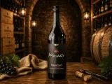 Butelka wina Primitivo Puglia na drewnianym stole, w tle piwniczka z winami, beczka i winogrona.