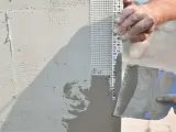 Mani esperte applicano stucco e rete per stuccare angolo muro, garantendo una finitura perfetta.