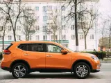 Pomarańczowy SUV do 50 tys. zaparkowany na tle białego budynku i drzew.