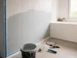 Rénovation de salle de bain : on est en train de repeindre le carrelage mural en gris. Matériel de peinture au sol.