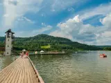 Słoneczny dzień nad zalewem Stara Morawa. Ludzie kąpią się, pływają na rowerach wodnych i odpoczywają na pomoście.