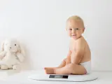 Uśmiechnięty chłopczyk w pieluszce siedzi na wadze. Chyba już czas na większy rozmiar, kiedy pampers jest za mały.