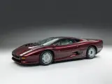 Bordowy Jaguar XJ220, ikona motoryzacji lat 90., prezentuje swoje aerodynamiczne linie na tle szarego tła.