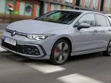 Szary Volkswagen Golf GTE porusza się po miejskiej drodze, z rozmytym tłem budynków i przechodniów.