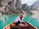 Uśmiechnięta kobieta siedzi w łodzi na turkusowym jeziorze, otoczona majestatycznymi górami **Dolomitów**.