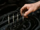Dłoń mechanika wykonuje wymianę świec żarowych w silniku diesla.