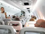 Widok wnętrza samolotu z pasażerami siedzącymi w rzędach i stewardesą.