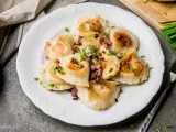 Talerz pełen pysznych, złocistych pierogów z bryndzą, posypanych skwarkami i szczypiorkiem. Idealne na obiad!