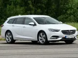 Vit Opel Insignia kombi parkerad vid en grönskande skog. En förare syns i bilen, kanske funderar på ett opel insignia problem.
