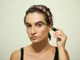 Dziewczyna z kwiatową opaską na włosach aplikuje żel do brwi. To świetny sposób na ich ujarzmienie i podkreślenie, a także może być pomocne co na porost brwi.