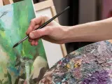 Main d'artiste peignant une scène verdoyante avec une peinture à l'acrylique. Palette de couleurs vibrantes.